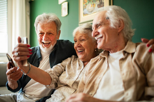 Smiling senior friends taking smartphone selfie at home