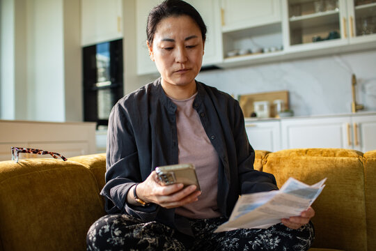 Concerned woman paying household bills on smartphone at home