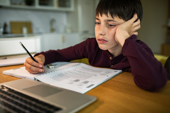 Tired boy studying homework with laptop at home