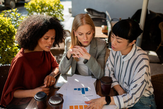 Three businesswomen discussing charts at outdoor cafe