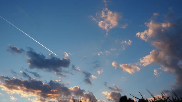 Plane flies through a colorful sky filled with pink and gray clouds during sunset. The scene captures the beauty of aviation and nature. Chemtrail in the sky. Conspiracy theory about chemtrails.