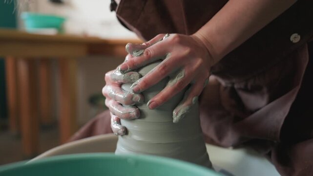 Pottery creation process. Group of craftsmen shaping tall ceramic pot on wheel in sunlight. Classroom environment where artisans collaboratively craft tall vessel with instructor support