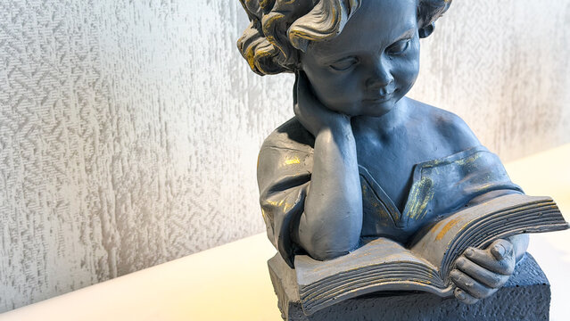 Decorative sculpture of a thoughtful child reading an open book in a modern interior, with textured neutral background and copy space. Concept of education, learning, reading and knowledge.