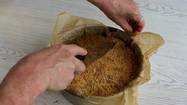 Hands cutting homemade crumb cake with a kitchen knife in a parchment-lined springform pan.
