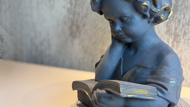 Decorative sculpture of a thoughtful child reading an open book in a modern interior, with textured neutral background and copy space. Concept of education, learning, reading and knowledge.