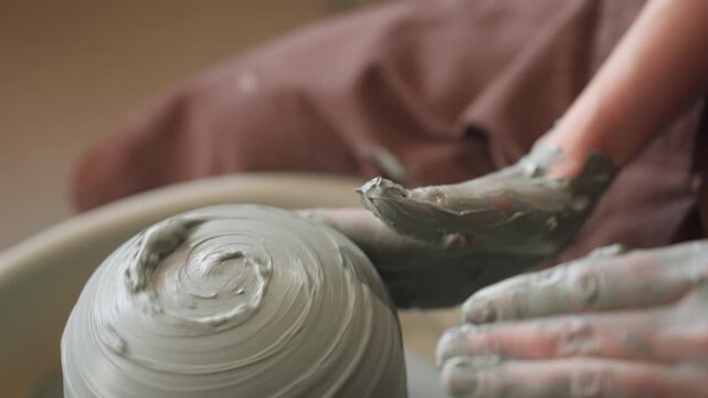 Potter forming bowl with hands. Wheel spins as hands mold wet clay. Creating spiral textures on wet clay with steady hands. Potter skillfully shapes spinning clay into textured bowl in studio