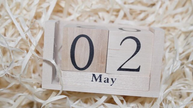 Wooden calendar blocks showing date May 2 on natural wood shavings background