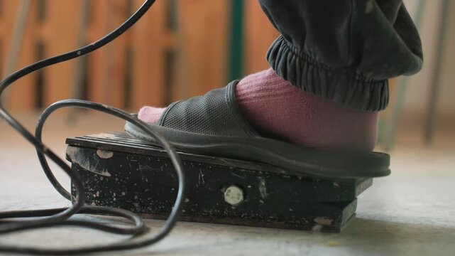 Foot on pottery wheel pedal, master potter presses wheel with socked foot for precise speed control, rapid rotation and focused studio intensity, glaze and kiln hinted in background
