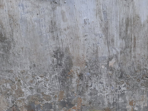 Grey concrete wall background texture with rough plaster brush strokes and weathered bottom patches.