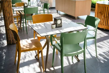 Fotobehang Horeca Colorful green and yellow chairs around tables in outdoor restaurant seating area, sunny summer resort with bamboo screens and patterned shadows  © Inga