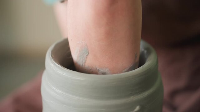 Focusing on hand forming ceramic cylinder. Clay is carefully molded into shape by hand on spinning wheel. Artisan expertly centers moist clay onto rotating pottery wheel with precise pressure