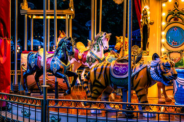 Colorful carousel horses and tiger figures illuminated at a night fair. © Khalil