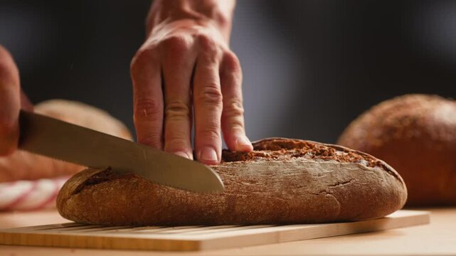 Bread rye loaf cut with knife by hand, fresh homemade sourdough on wooden board, close-up macro shot
