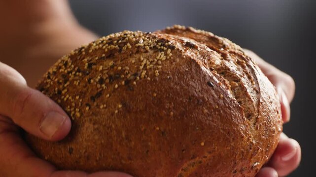 Bread loaf Spanish round bread with seeds, held in hands on checkered cloth, close-up macro shot