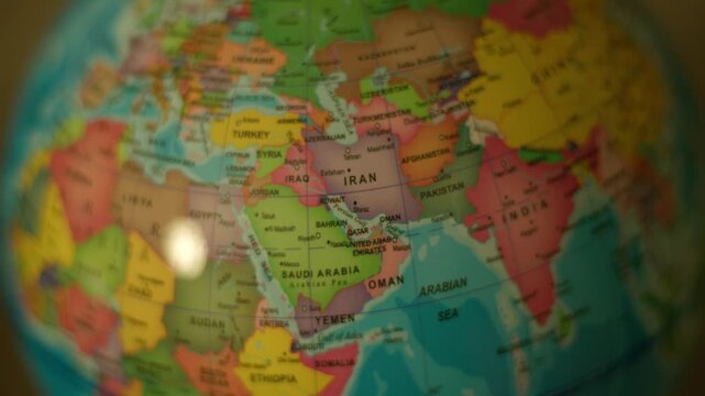 Close-up globe spins, highlighting Middle East countries. Soft light glints off surface, creating gentle reflections. Vibrant colors define continents, making geography visually engaging