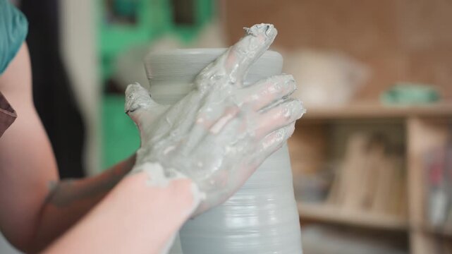 Delicate rim shaping on spinning wheel with mudcovered hands, studio shelves blurred in background, careful pressure forming lip and profile, quiet moment of finishing and satisfaction in craft