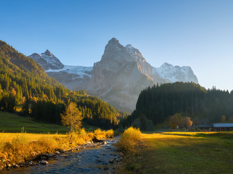 Sunset light shines on Rosenlaui river in Switzerland. Sun rays and glow illuminate flowing water and rocks in alpine gorge.