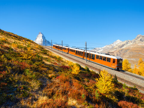 Passenger train on a railway in Zermatt, Switzerland. Autumn nature in the Alps. Train passes through autumn forest with Matterhorn peak in background.