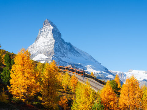 Passenger train on a railway in Zermatt, Switzerland. Autumn nature in the Alps. Train passes through autumn forest with Matterhorn peak in background.