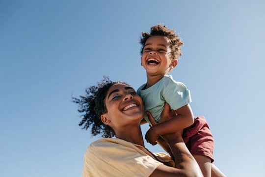 Smiling mother lifting laughing child outdoors in blue sky for family background and joyful lifestyle banner