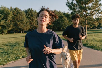 Obraz premium Active young woman and man jogging with dog on park path for fitness lifestyle background and outdoor exercise scene