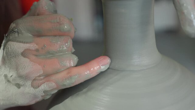 Artist carefully sculpts clay on wheel. Craftsman meticulously shapes pottery using fingers and sponge. Master potter skillfully refines pottery form through precise movements and tools