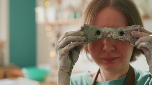 Playful potter smiles after shaping clay. Artist happily displays hands covered in wet clay on set. Creative individual generously enjoys satisfaction of crafting with mud and clay