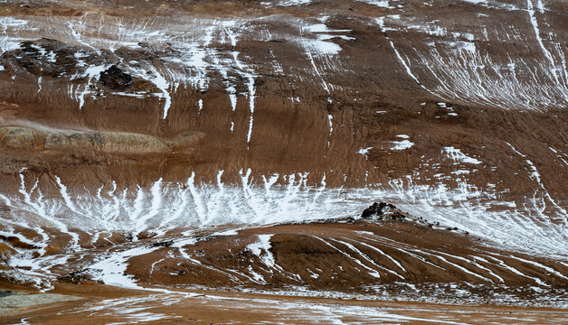 Reddish brown mountain slope showing melting snow patches and ice formations. Nature background. Iceland icelandic landscape
