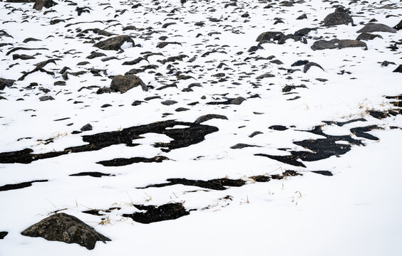 Melting snow reveals dark rocks and ground forming a natural, abstract pattern on a winter landscape