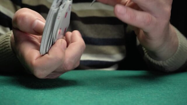 Hands of a male card player in a striped sweater shuffle a deck of playing cards on a green felt table, showcasing the fluid motion of card manipulation in a focused setting