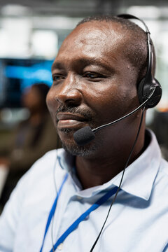 Happy technician analyzes system diagnostics on a computer during a support call, speaking through a headset microphone and resolving technical issues remotely from an office workstation.