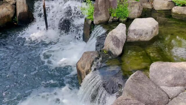 Clear fresh water cascades over smooth rocks into a peaceful pond, creating foaming splashes and gentle ripples