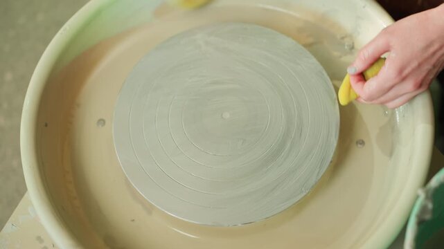 Hands finishing pottery wheel surface, maker performs final rinse and wipe with sponge, delicate edge trim and cleanup reveal subtle glaze traces, precise steady motions in professional studio