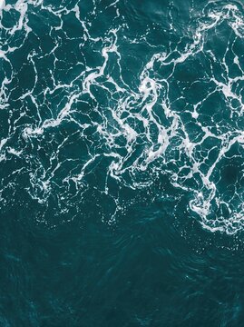 Fine lace sea foam over deep teal water from above