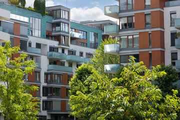 Modern residential apartment buildings with balconies and large windows surrounded by lush greenery...