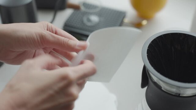 Woman holds paper coffee filter beside pour over dripper on kitchen counter