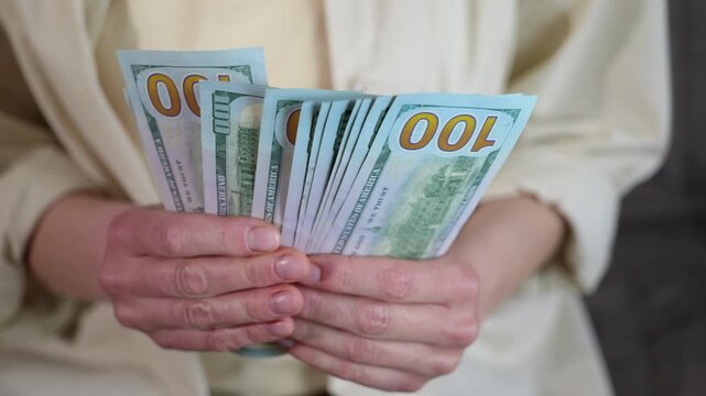 Woman's hands holding a wad of hundred dollar bills. Hands of a woman holding a large amount of cash, fanning out a stack of one hundred dollar bills representing wealth, financial success