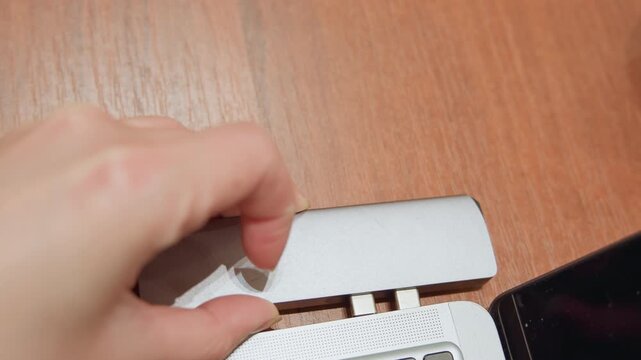 Aluminum hub aligning with laptop ports, hands of technician carefully seating multiport adapter into laptop edge on workbench, precise alignment, inspection and calibration during repair workflow,