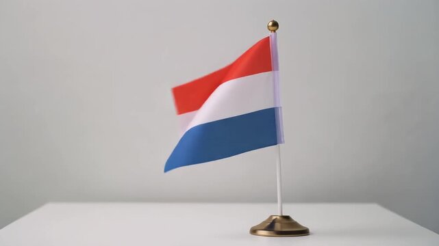 Small Netherlands Flag Waving on White Table Desk Stand Isolated on Grey Background