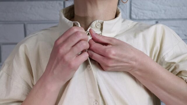 Woman unbuttoning her cotton shirt collar. Unrecognizable woman unbuttoning her beige casual cotton shirt, revealing her neck and clavicle