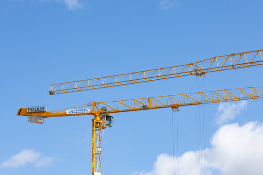 Two yellow construction cranes against a blue sky with white clouds, showcasing their long arms and elevated positions on a construction site