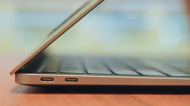 Closeup laptop lid closing on desk, soft bokeh background, usb ports visible, matte gold chassis, gentle hinge motion, hand reaching to close device, calm remote work wind down, modern minimalist