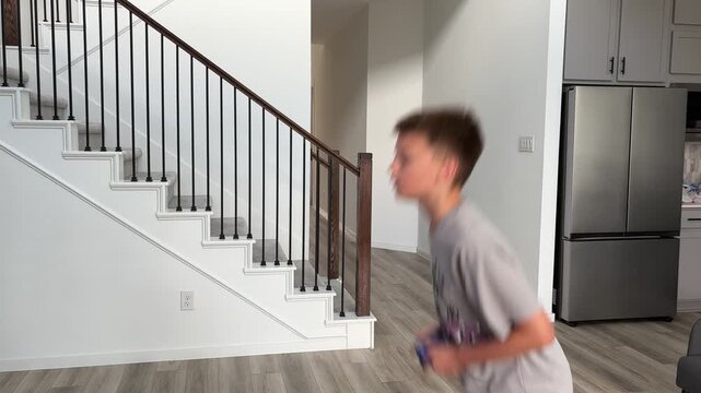 A boy actively jumping and moving while intensely engaged in a video game, operating a blue controller in a modern home. 4K horizontal video.