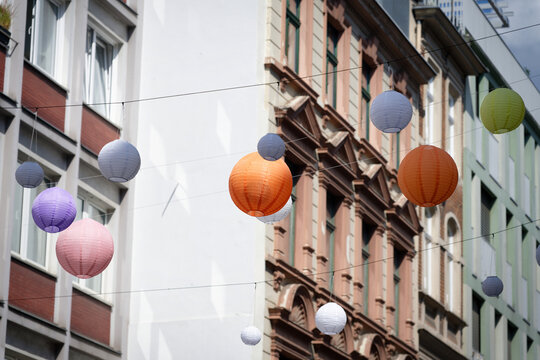 Colorful round paper lanterns hanging across a shopping street between urban building facades in Cologne