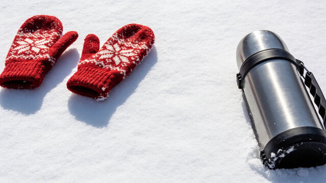 Red knitted mittens and thermos on fresh snow in winter light