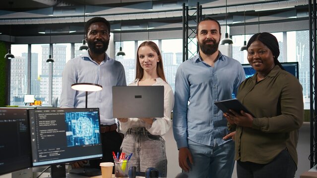 Smiling programmers collaborate in an office, using AI automation to optimize performance, forecast technical issues and train machine learning models while working together on multiple devices.