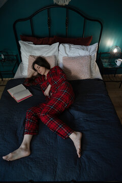 Woman sleeping beside open book on bed, overhead view
