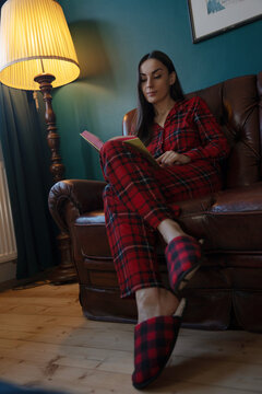 Woman reading in armchair wearing pajamas and slippers
