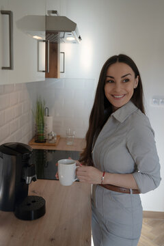 Smiling woman holding fresh coffee in modern kitchen