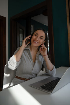 Smiling professional woman on phone beside laptop at home